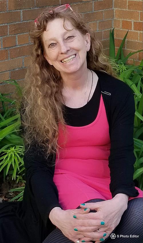 Photo of Heidi Kaminski, long curly blond hair, pink glasses atop her head, a bright pink dress and black sweater and tights 